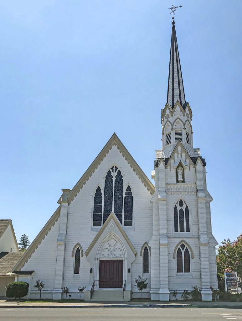 White church with a tall steeple against a clear blue sky, representing the congregations Bushore Church Real Estate serves throughout California.